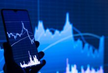 a person holding a cell phone in front of a stock chart