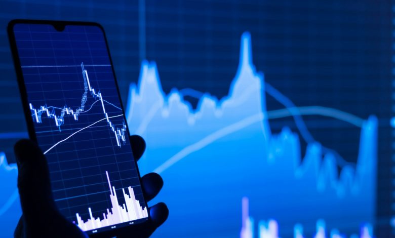 a person holding a cell phone in front of a stock chart